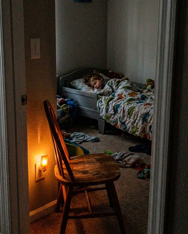 Chair by the door of a toddler's room, boy asleep in his bed